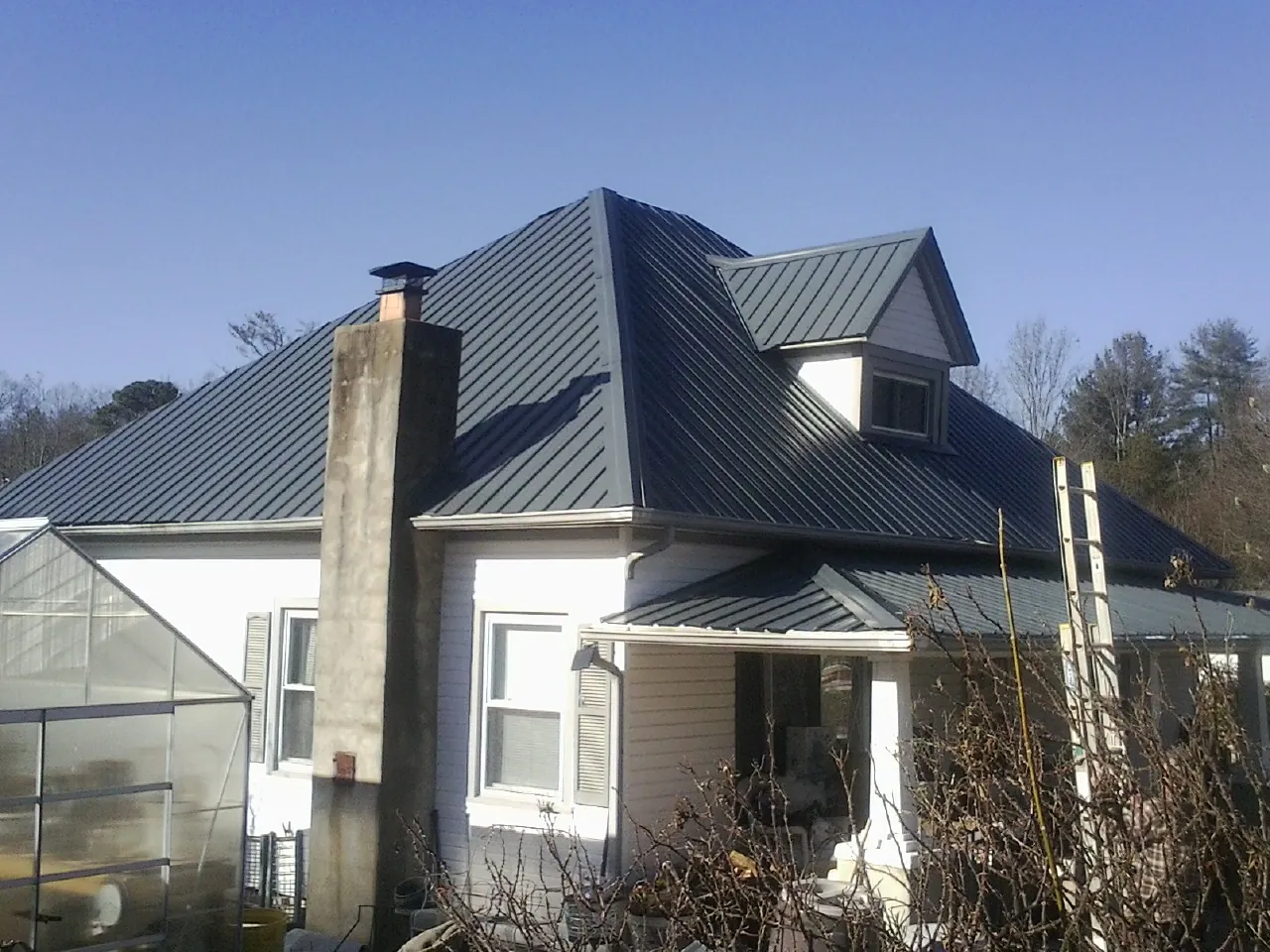 Dark blue standing seam metal roof on a white farmhouse with dormer in Yorktown